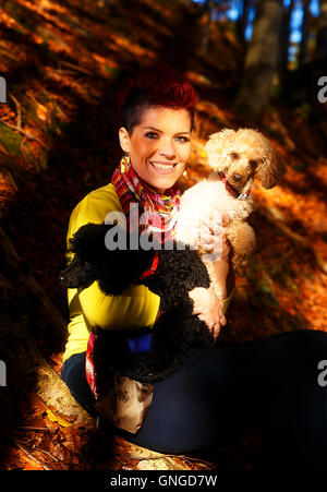 Ragazza carina con il bianco e nero cane sorridente e abbracciando presso la foresta di autunno all'esterno. Contatto con gli occhi. Foto Stock