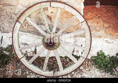 Vecchia ruota in legno si erge nei pressi di pietra parete rurale Foto Stock