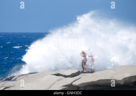 Due donne in piedi sulle rocce colpito dalla grande onda, Corsica, Francia Foto Stock