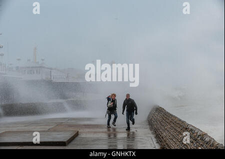 Un paio di eseguire per sfuggire le onde sul lungomare di Brighton Foto Stock