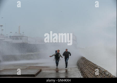 Un paio di eseguire per sfuggire le onde sul lungomare di Brighton Foto Stock