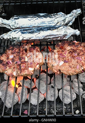 Hamburger e stagnola avvolto sulla pannocchia di mais di essere cucinati su un carbone di legna per barbecue Foto Stock