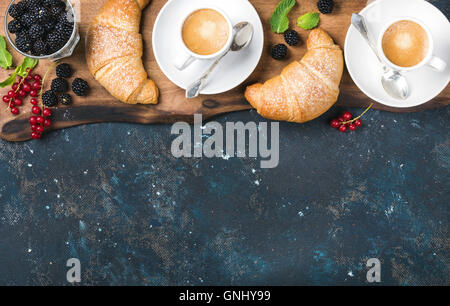 Set colazione. Croissant appena sfornati con giardino di bacche e di tazze da caffè rustico di legno più scuro legno compensato di grunge indietro Foto Stock