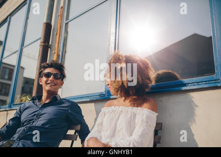 Colpo di giovane uomo e donna seduta all'aperto e parlare. Coppia giovane di trascorrere del tempo insieme. Foto Stock