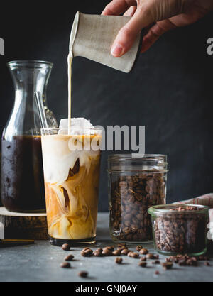 Donna versare il latte in un caffè ghiacciato Foto Stock