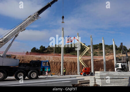 Sito in costruzione, gru e camion lavorare con colonne di cemento Foto Stock