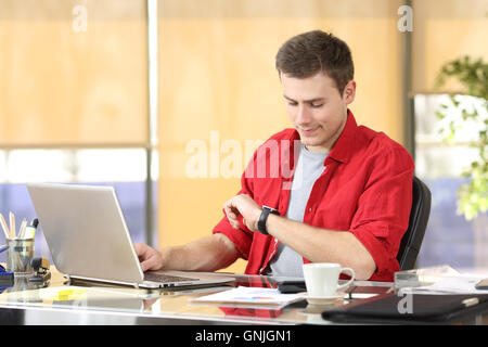 Uomo d'affari di lavoro e di controllo smart watch orologio o seduti in un desktop in ufficio Foto Stock