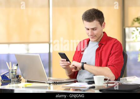 Imprenditore di avvalersi della consulenza di un orologio intelligente e telefono cellulare seduti ad una scrivania in ufficio Foto Stock