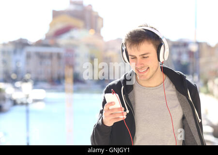 Vista frontale di un adolescente di camminare verso la telecamera in ascolto di musica con le cuffie da smart phone in una destinazione di vacanze Foto Stock