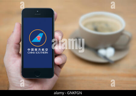 Un uomo guarda al suo iPhone che visualizza la China Southern Airlines logo, mentre sat con una tazza di caffè (solo uso editoriale). Foto Stock