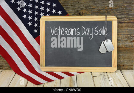 Veterani giorno Vendita segno sulla lavagna nera con dog tags militari e bandiera americana. Foto Stock