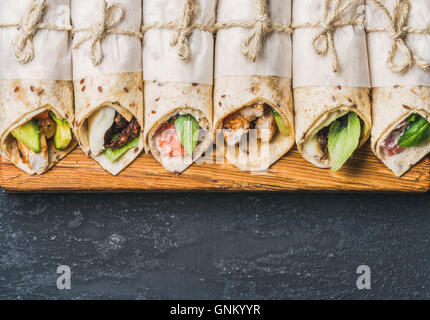 Tortilla avvolge con diversi riempimenti su grigio scuro dello sfondo in calcestruzzo Foto Stock