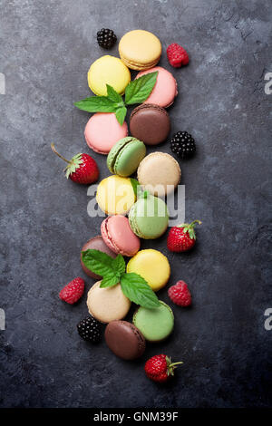 Amaretti colorati e bacche sul tavolo di pietra. Dolce macarons con fragola, lampone e Blackberry. Vista superiore Foto Stock