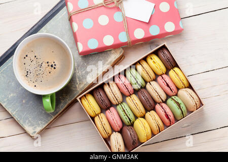 Amaretti colorati in una confezione regalo e una tazza di caffè sul tavolo di legno. Dolce macarons. Vista superiore Foto Stock