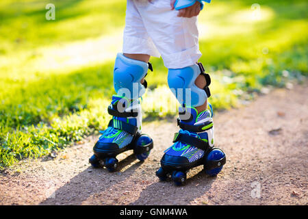 Bambina learning per pattino a rotelle in sunny summer park. Bambino di indossare la protezione del gomito e del ginocchio pad, protezioni del polso e la sicurezza Foto Stock