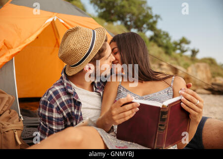 Ritratto di una coppia felice seduto alla tenda e baciare durante l'utilizzo di tablet pc e libro di lettura Foto Stock