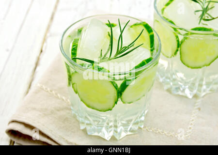 La limonata con un cetriolo e rosmarino in due glassful sul tovagliolo beige contro lo sfondo delle tavole di legno Foto Stock