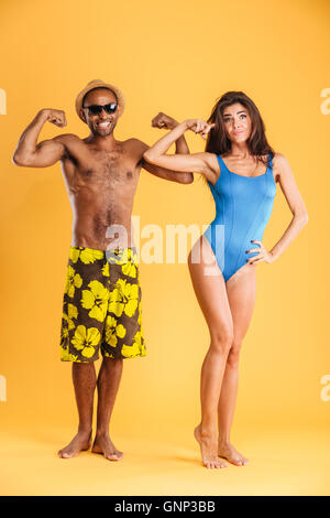 Giovani afro american uomo e donna bella mostra bicipite isolato su sfondo arancione Foto Stock