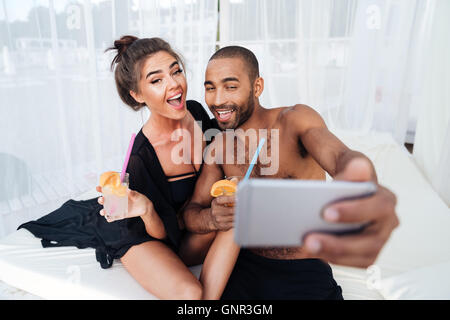 Sorridenti multirazziale giovane rendendo selfie holding e cocktails presso la spiaggia Foto Stock