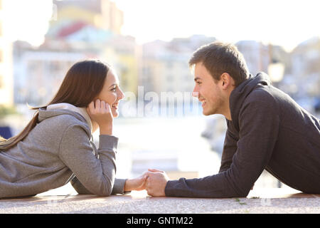 Vista laterale di un paio di adolescenti dating e flirtare Falling in Love cercando ogni altro sdraiato sul pavimento in un porto Foto Stock