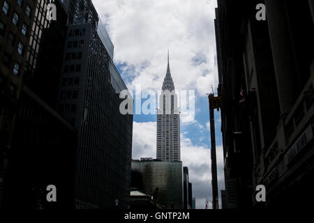 Ben illuminata, iconico Chrysler Building incorniciato da edifici scuro sul New York per le strade delle città Foto Stock