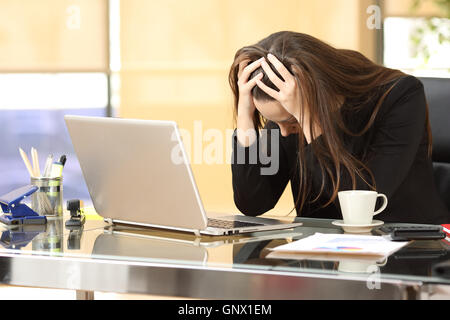 Imprenditrice disperata sulla linea preoccupato dopo il fallimento di fronte a un computer portatile con le sue mani in testa in ufficio Foto Stock