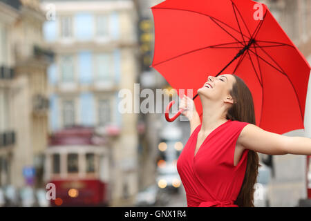 Ritratto di una donna felice che indossa camicia rossa sotto un ombrello per respirare la strada e la città vecchia in un giorno di pioggia Foto Stock