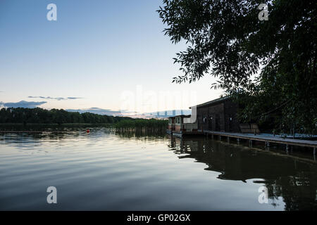 Il panorama su un lago con alberi e boatshouse Foto Stock