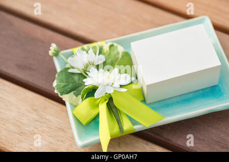 Una piccola casella bianca su decorate turchese Vassoio in ceramica con fiori di colore bianco e nastro verde Foto Stock