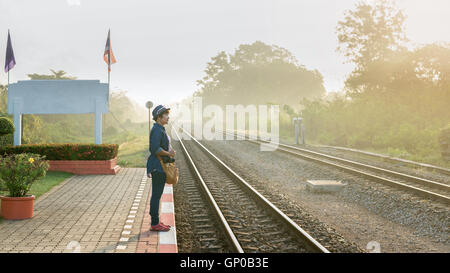 In una nebbiosa giornata di sole un donne asiatiche i viaggiatori in attesa di un treno sulla piattaforma a livello locale stazione ferroviaria. Copia dello spazio. Foto Stock