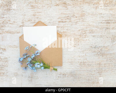 Carta marrone busta bianca con la scheda vuota e dimenticare blu-me-non bouquet di fiori legati con corda di iuta sul rustico di vernice bianca Foto Stock