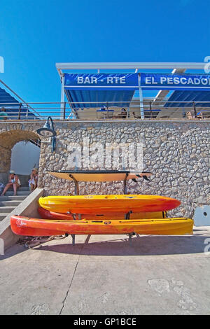 Plastica impilate le canoe e El Pescador ristorante sul molo su una soleggiata giornata estiva in agosto 5 in Sant Elm, Mallorca, Spagna. Foto Stock