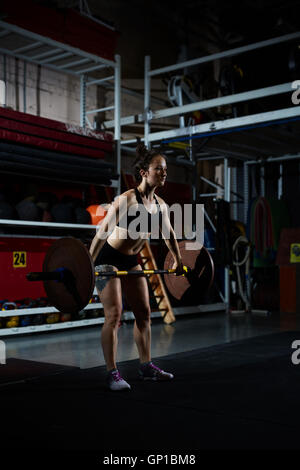 Forte giovane donna con barbell in piedi in palestra Foto Stock