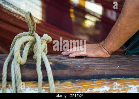 Fisherman's mano con rete da pesca in background. Bagnato e rugosa mano appoggiata su una barca di legno di recinzione. Foto Stock