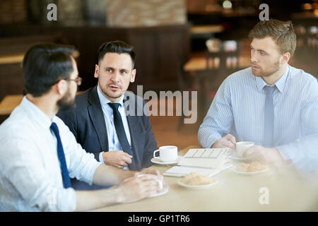 Tre uomini di affari in abbigliamento formale sulla riunione informale nella caffetteria con caffè e la condivisione di idee. Foto Stock