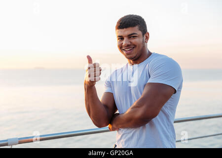 Allegro americano africano giovane atleta e permanente che mostra i pollici fino all'aperto Foto Stock