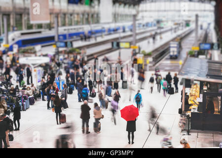 Donna con ombrello rosso in attesa alla stazione ferroviaria e sfocata persone in movimento, solitudine concept Foto Stock