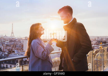 Coppia felice bevendo champagne e sorridente al tramonto a Parigi, celebrazione Foto Stock