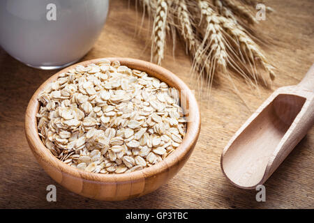 Fiocchi d'avena (fiocchi di avena), latte e dorate spighe di grano su sfondo di legno. Cibo crudo ingredienti, uno stile di vita sano, la cottura di cibo Foto Stock