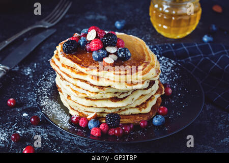 Deliziosi pancake con frutti di bosco freschi e miele su ardesia scura, sfondo vista ravvicinata Foto Stock