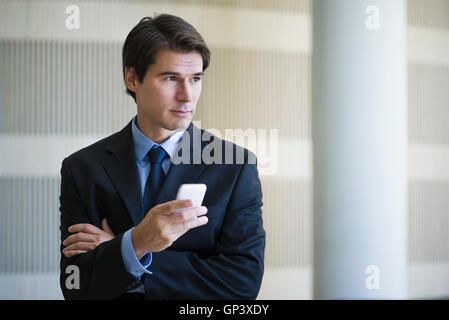 Imprenditore utilizza lo smartphone, guardando lontano nel pensiero Foto Stock