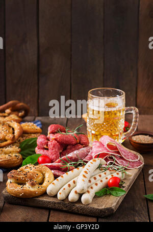 Bicchiere di birra, salatini e vari insaccati su sfondo di legno. Oktoberfest. Foto Stock