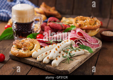 Bicchiere di birra, salatini e vari insaccati su sfondo di legno. Oktoberfest. Foto Stock