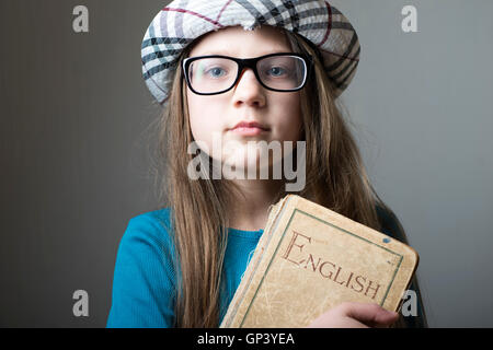 Grave la ragazza di occhiali e cappello a scacchi con libro inglese in mani Foto Stock