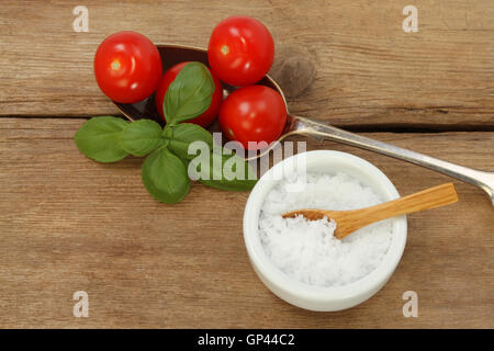 Pomodori e basilico in un cucchiaio sul vecchio legno rustico con seasalt in un ramekin Foto Stock