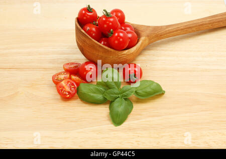 Pomodori in un cucchiaio di legno con basilico su un tagliere di legno Foto Stock