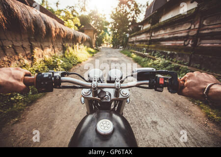 Biker alla guida della sua moto sulla strada di campagna in un villaggio. Il punto di vista con il focus è sul manubrio e man mano. Foto Stock