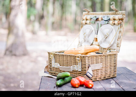 Aprire il cestino da picnic con pomodori, cetrioli e pane su una tavola di legno nel parco. Foto Stock