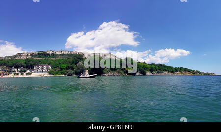 La vacanza estiva lo sfondo con un hotel in riva al mare e una barca galleggia sull'acqua. Vista panoramica della costa di Black S Foto Stock