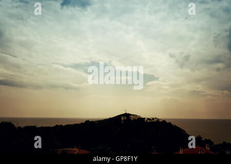 La silhouette di una santa croce cristiana illuminata dalla luce del sole sulla cima di una collina su un drammatico cielo nuvoloso. Bella vista sul Foto Stock